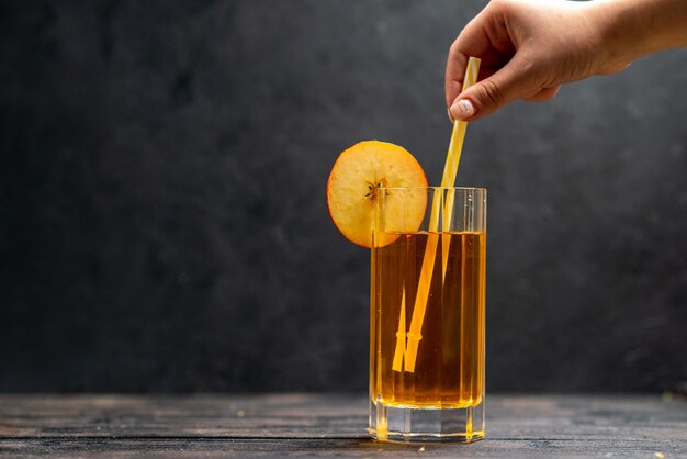 Front close up view of fresh natural delicious juice in a glass and hand holding tube in it on black background