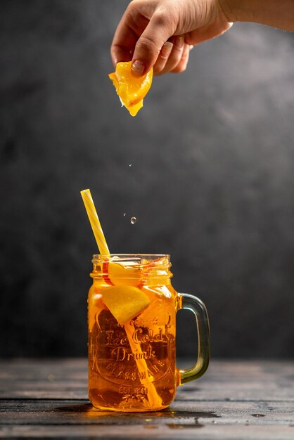 Вид спереди крупным планом свежего натурального вкусного сока в стакане, рука положить апельсиновый лайм с трубкой в нем на черном фоне