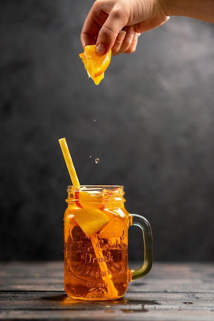 Front close up view of fresh natural delicious juice in a glass hand putting orange limes with tube in it on black background