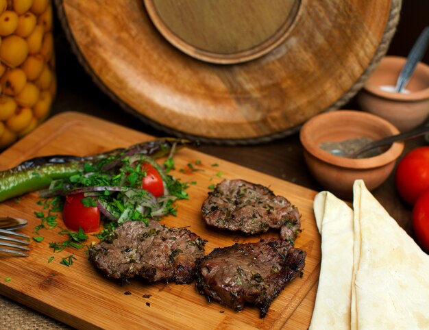 Вид спереди крупным планом жареные кусочки мяса вкусные вместе со свежими овощами на коричневом деревянном столе