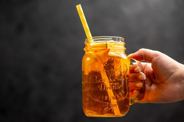 Вид спереди крупным планом руки, держащей стакан свежего натурального вкусного сока с трубкой в нем на черном фоне
