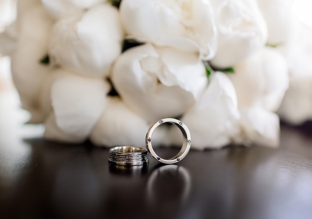 Front close up view of two wedding rings lying on the peonies bouquet background
