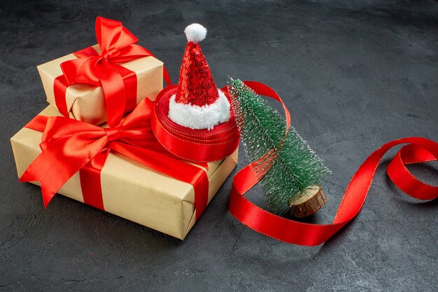 暗いテーブルに赤いリボンとサンタクロースの帽子のクリスマスツリーと美しい贈り物の正面のクローズビュー