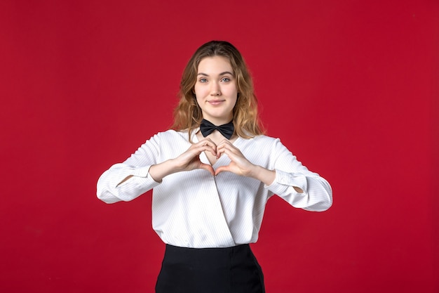 Front close view of beautiful smiling waitress woman butterfly on the neck and making heart gesture on red background