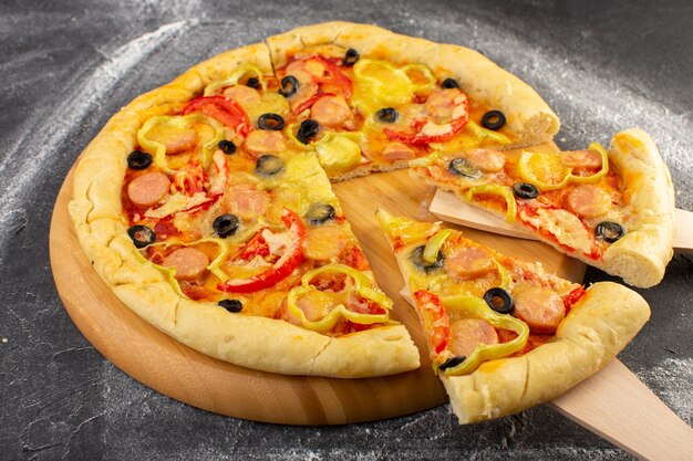 暗い机の上の赤いトマト、ブラックオリーブ、ベルペッパー、ソーセージの正面の近くのチーズのピザ