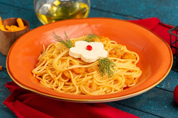 Вид спереди крупным планом приготовленные итальянские макароны с зеленью внутри оранжевой тарелки с маслом и овощами на синем