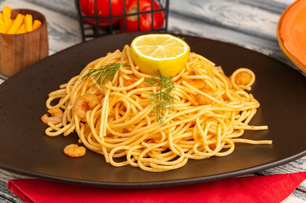 Front close view cooked italian pasta with shrimps greens and lemon inside brown plate on grey