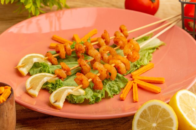 Front close view cooked shrimps on sticks inside peach plate with lemon slices green salad oil