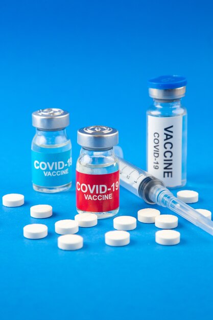 Front close view of COVID- vaccines in medical ampoules pills disposable syringe on dark and soft blue background