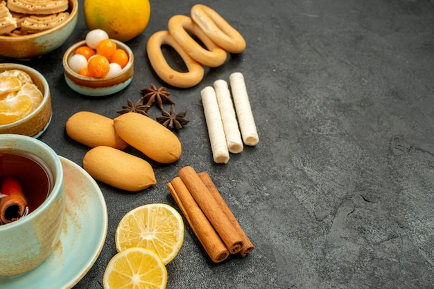 Front close view cup of tea with candies biscuits and fruits on grey table tea sweet cookie