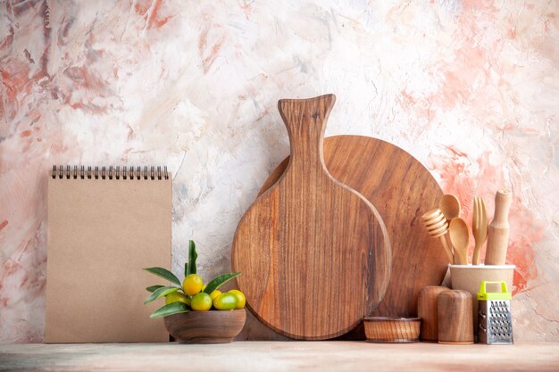 Front close view of cutting board wooden spoons grater kumquats in pot and notebook on colorful surface