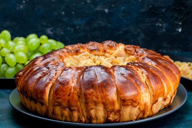 Вид спереди крупным планом вкусный запеченный торт с изюмом и свежим зеленым виноградом на темно-синей поверхности торт пирог сахарное сладкое бисквитное тесто