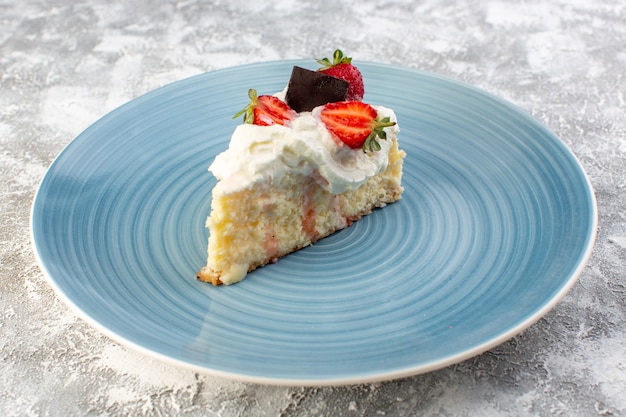 Front close view delicious cake slice inside blue round plate with cream and strawberries on the grey surface