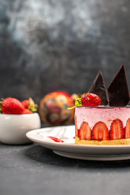 Front close view delicious cheesecake with strawberry and chocolate on oval plate bowl of strawberries