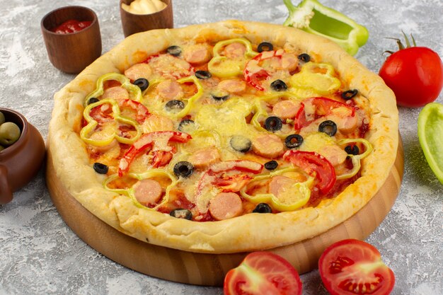 Front close view delicious cheesy pizza with olives sausages and tomatoes on the grey surface