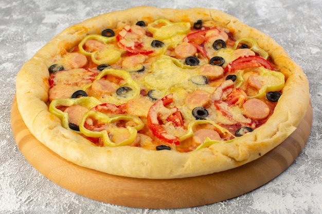 Front close view of delicious cheesy pizza with olives, sausages and tomatoes on the grey surface
