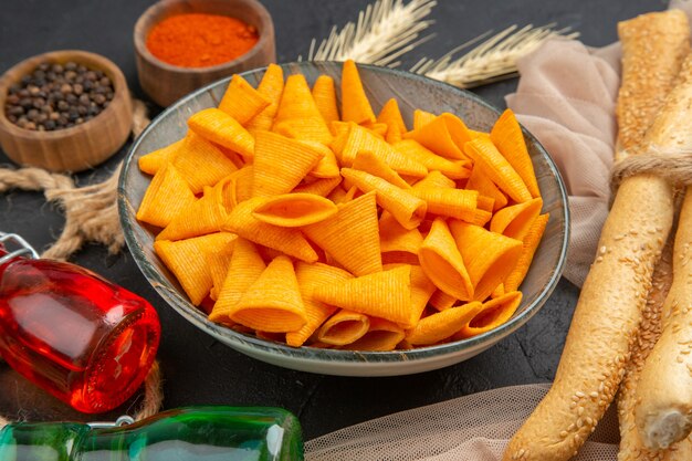 Front close view of delicious chips fallen bottles peppers on towel and rope on a black background