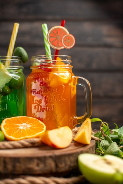 Front close view of delicious fresh juices and fruits on a wooden tray on a brown background