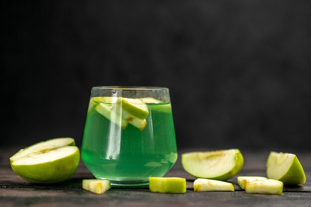 Front close view of delicious juice in a glass and an chopped apple on dark background