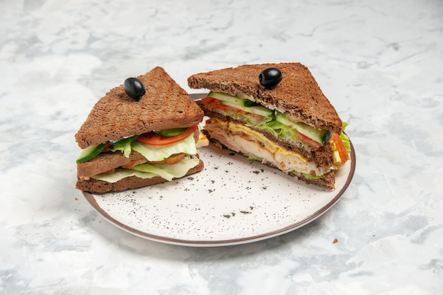 Front close view of delicious sandwich with black bread decorated with olive on a plate on stained white surface