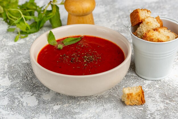 Front close view delicious tomato soup with bread rusks and greens on grey, soup meal dinner vegetable