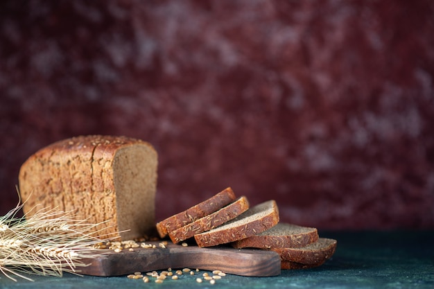 Front close view of dietary black bread spikes wheats on wooden cutting board on blue maroon mixed colors background