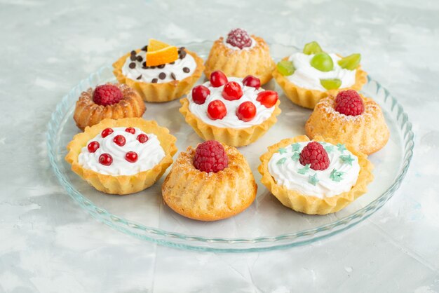 Front close view different cakes with cream and fresh fruits on the light surface cookie sugar sweet