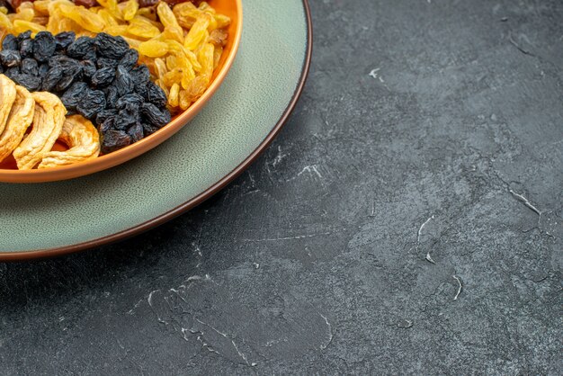 Front close view dried fruits with raisins inside plate on a dark grey space