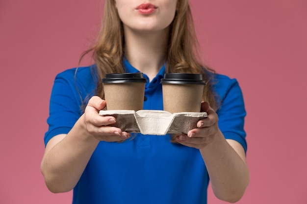 ピンクのデスクサービスの制服で茶色のコーヒーカップを配達する青い制服を着た正面の女性の宅配便会社の仕事を届ける