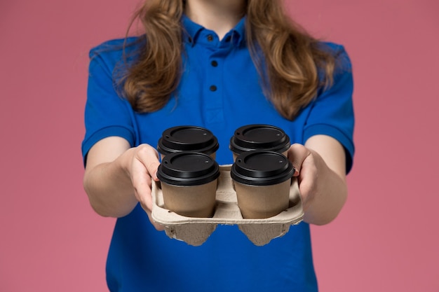 Free photo front close view female courier in blue uniform delivering brown delivery coffee cups on pink desk service uniform company worker