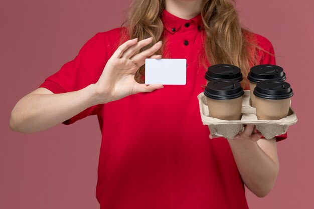 ピンクの制服のサービスワーカーに茶色の配達コーヒーカップとカードを保持している赤い制服の正面の女性の宅配便