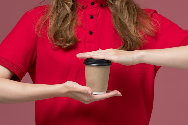 Front close view female courier in red uniform holding coffee cup on the pink, uniform service