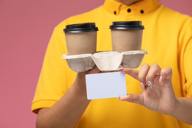 분홍색 책상 유니폼 배달 여성 색상에 플라스틱 갈색 커피 컵과 카드를 들고 노란색 유니폼 노란색 케이프에 전면 닫기보기 여성 택배