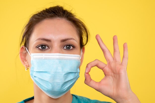 Front close view female doctor in sterile mask on yellow background