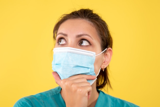 Front close view female doctor in sterile mask on yellow background