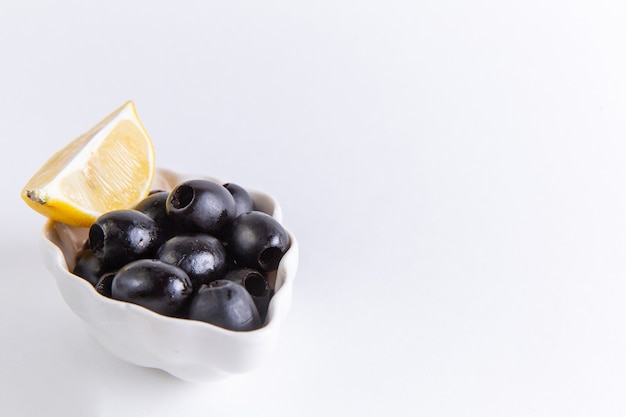 Front close view fresh black olives with lemon slice on white surface color photo food vegetable oil