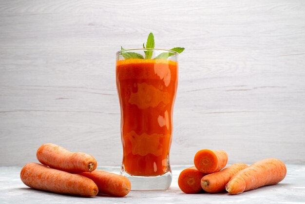 Вид спереди крупным планом свежий морковный сок внутри длинного стакана с листьями и вместе со свежими овощами моркови