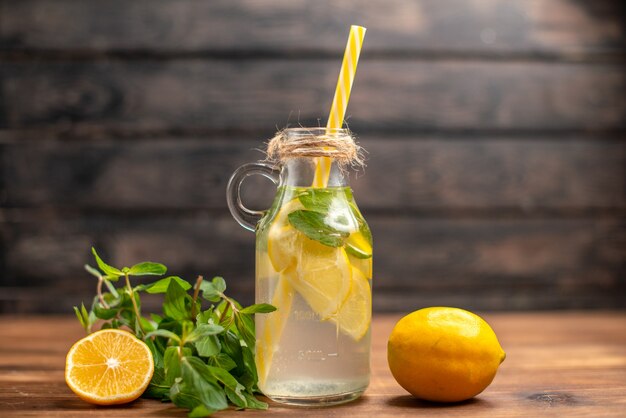 Front close view of fresh detox water served with tube mint and orange on a brown background