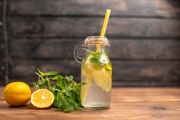 Front close view of fresh detox water served with tube mint and orange on the right side on a brown background