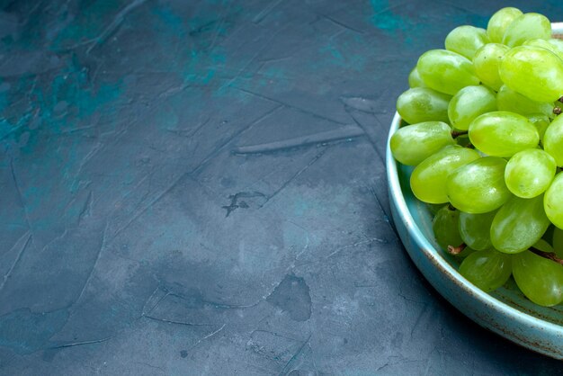 Front close view fresh green grapes mellow and juicy fruits inside plate on the dark-blue desk.