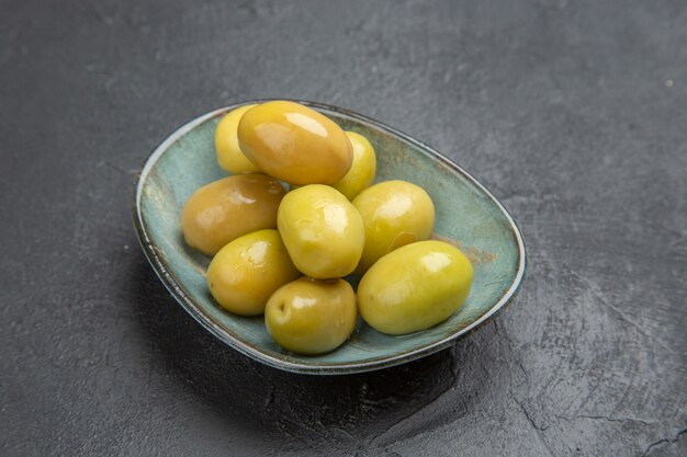 Front close view of fresh organic green olives on a blue plate on a black background