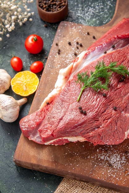 Front close view of fresh raw red meat on wooden cutting board on nude color towel lemon garlic on mixed color background