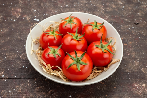 Front close view fresh red tomatoes inside white plate on the wooden brown background vegetable fruit color