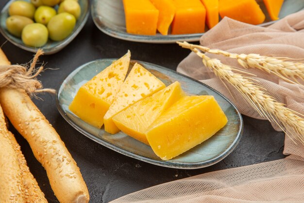 Front close view of fresh tasty chees slices on a towel and green olives on a black background