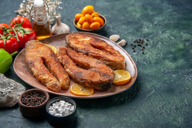 Vista frontale ravvicinata di pesce fritto e fette di limone su un piatto marrone spezie pomodori olio bottiglia sul tavolo colori mix con spazio libero