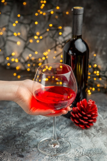 Вид спереди крупным планом руки, держащей бокал сухого красного вина и бутылку на сером фоне