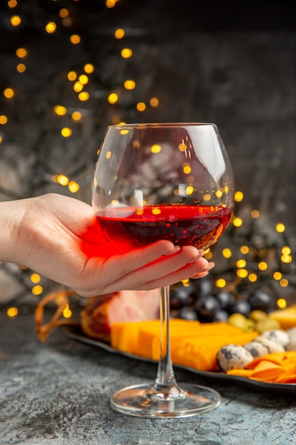 Front close view of hand holding a glass of dry red wine and deicious snack on gray background