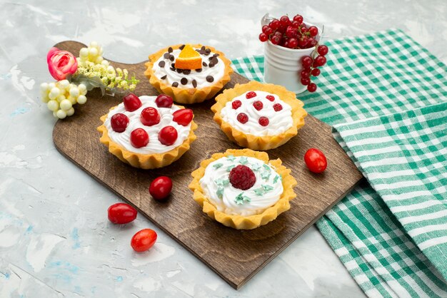 Front close view little cream cakes with fruits on the light grey desk 