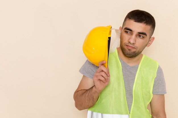 Front close view male builder holding yellow protective helmet on light background