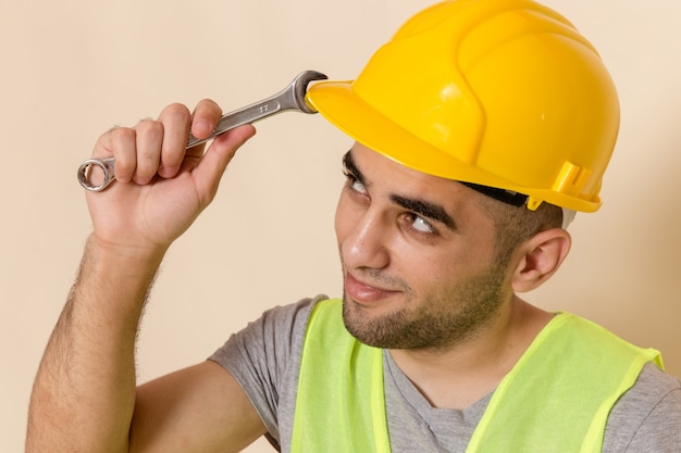 Front close view male builder in yellow helmet posing with tool on light background
